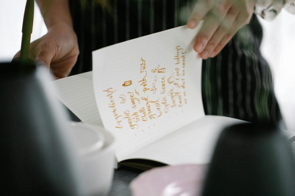 Closeup of hands turning a page with handwritten ingredients in a cookbook.