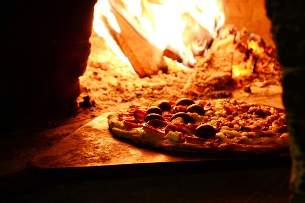 Delicious pizza baking in a traditional wood-fired oven with vibrant flames.